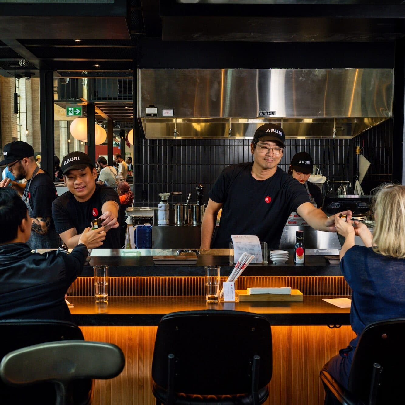 Sushi chefs passing hand rolls to customers who are sitting at the chef's table.