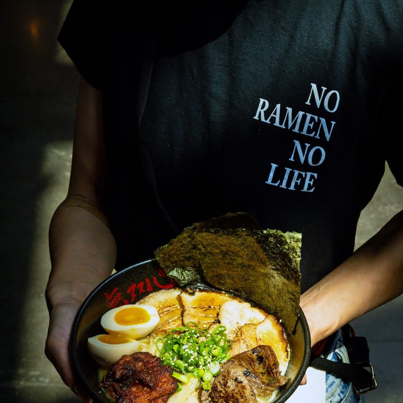 Employee wearing a t-shirt that says, No Ramen, No Life, holding a bowl of ramen noodles