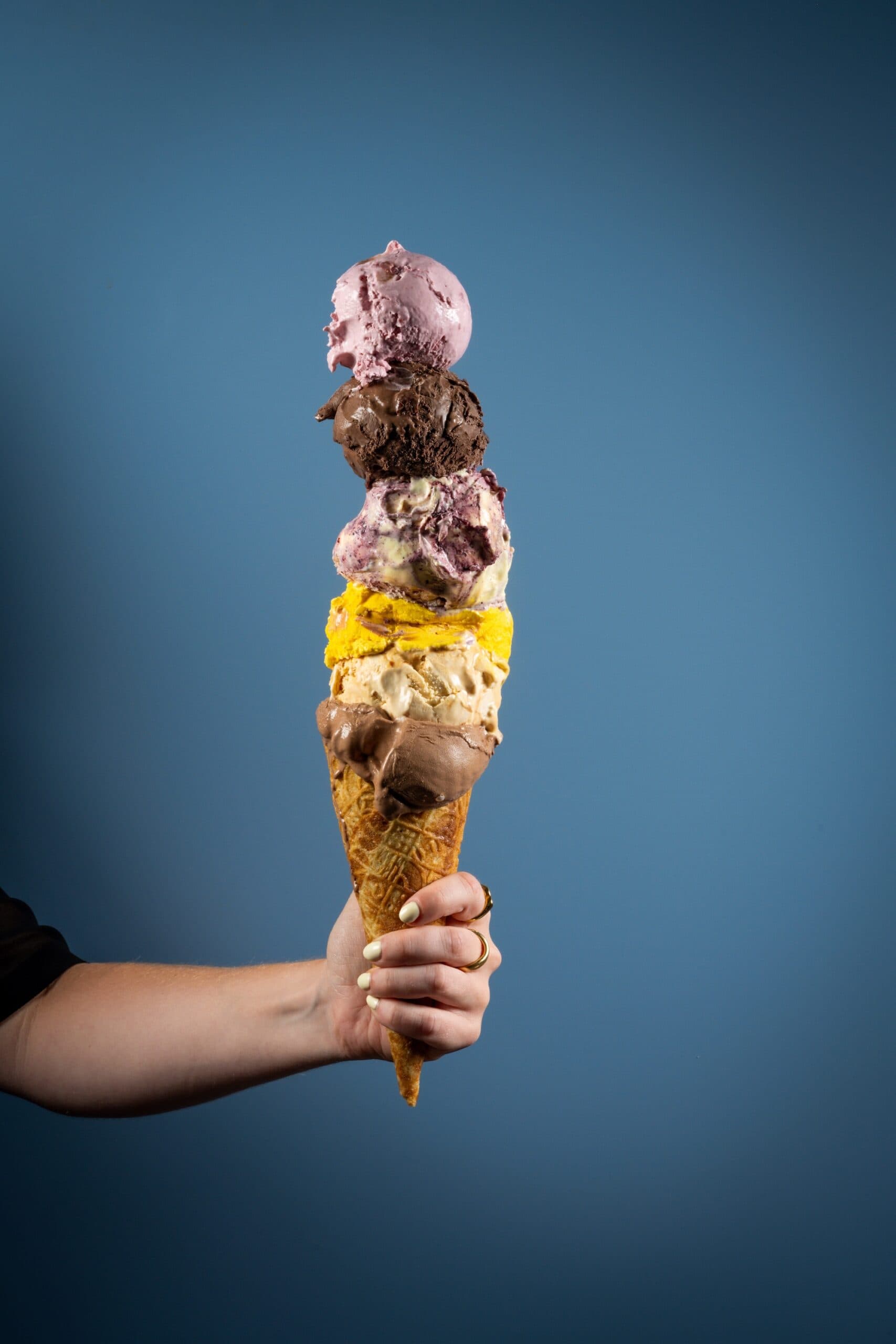 Hand holding six scoops of ice cream on a waffle cone