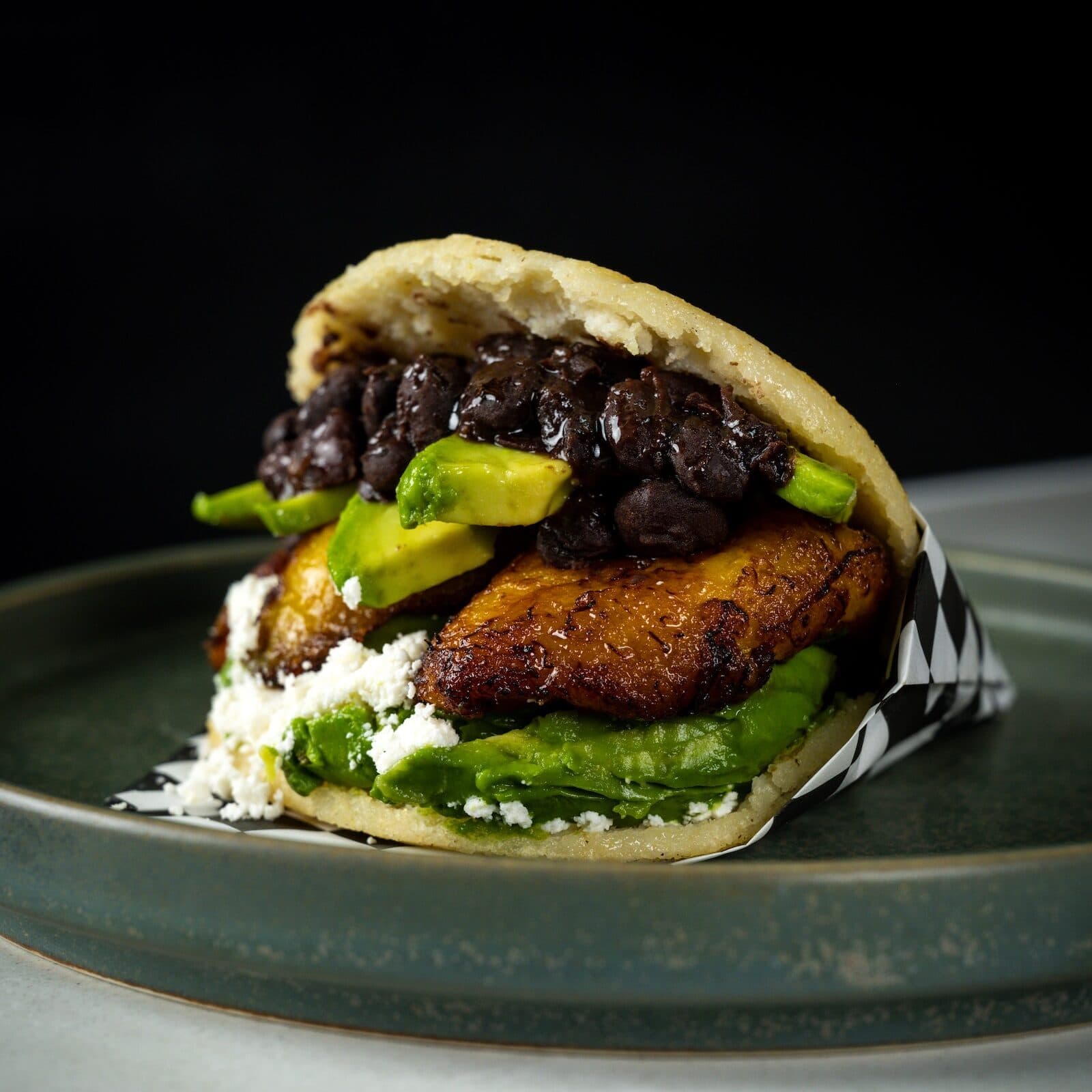 Bean based arepa with avocado and plantain on a green stoneware plate