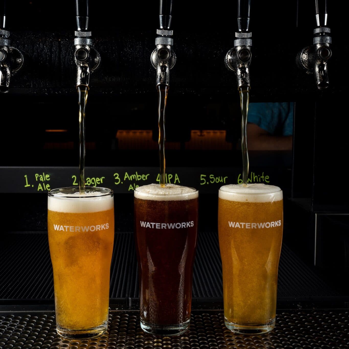 Pale ale, lager and amber ale draft beer being poured into three beer glasses.