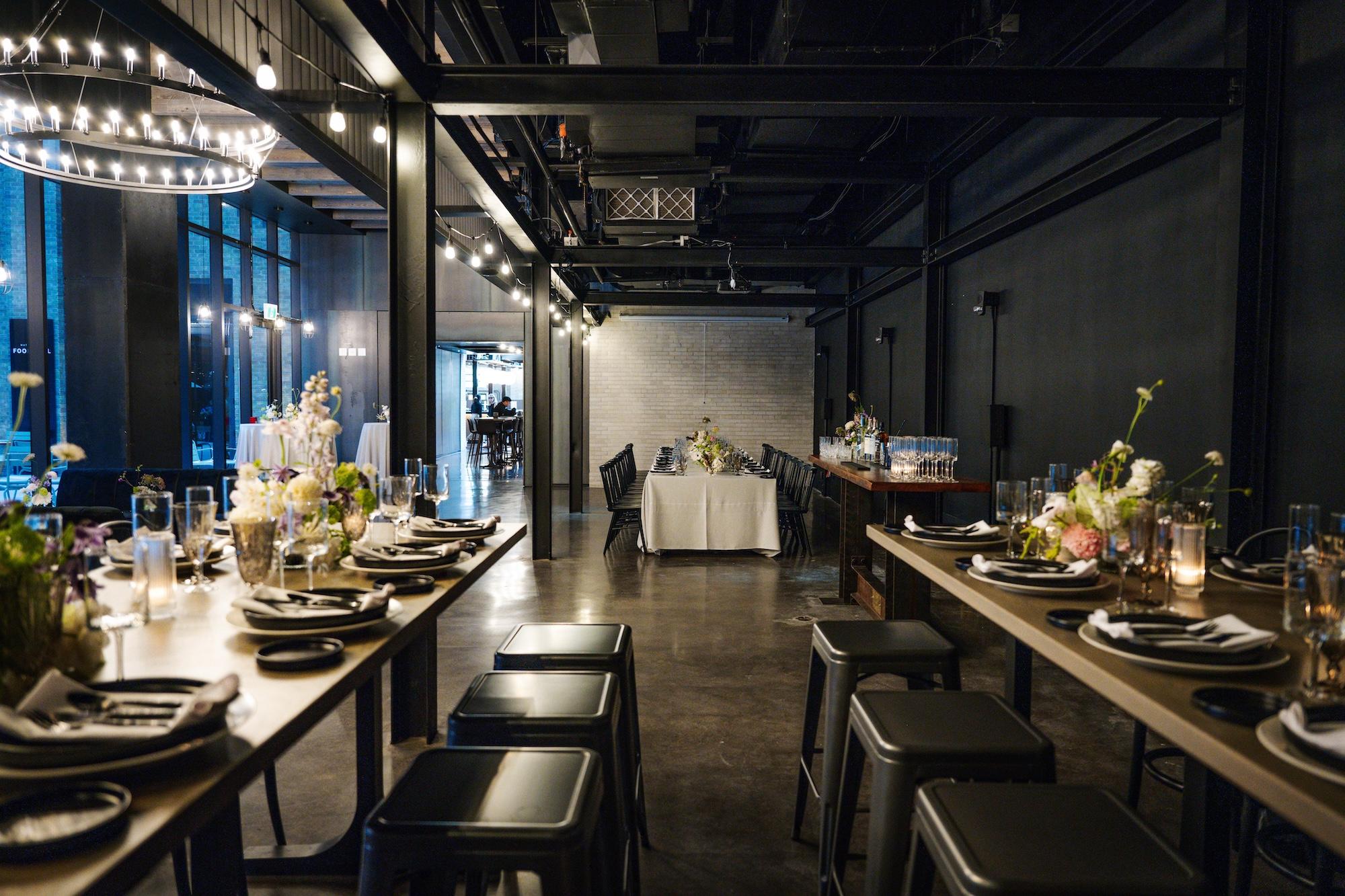 Tables set for a casual dinner in an industrial setting of heritage brick, polished concrete floors and steel beams.