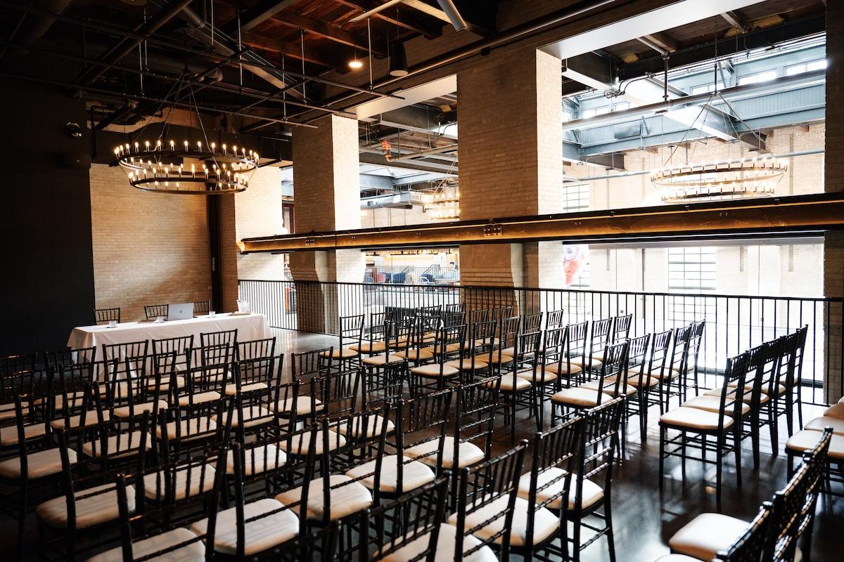 A meeting set up showing rows of chairs in front of a speaker table. The upper level of the food hall is visible beyond the east hall railings.