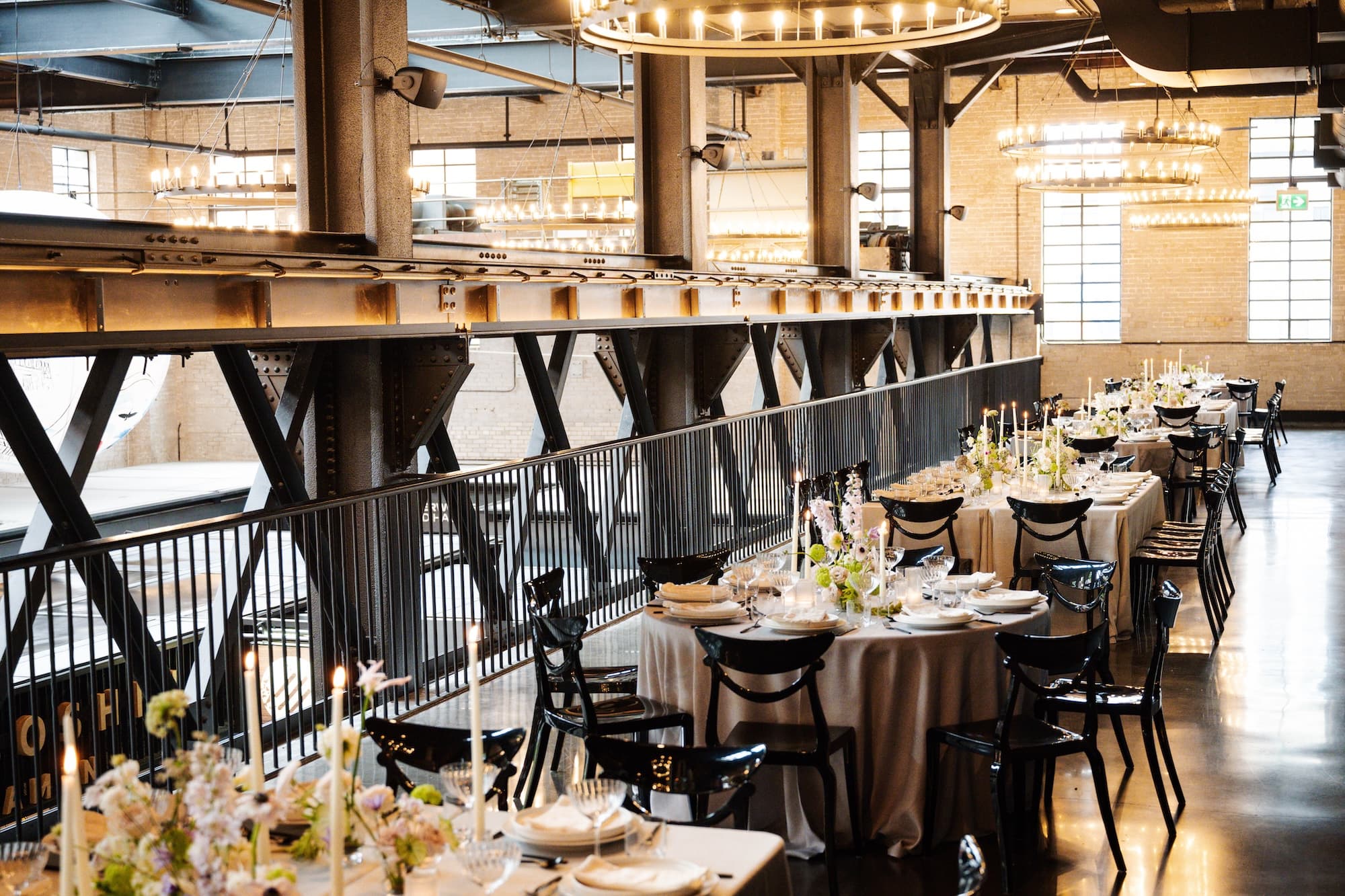 Seated dinner layout in the West Hall Event Space. Round and rectangular tables with light gray linens, organic flower arrangements and tapers candles, are set for over 70 guests.