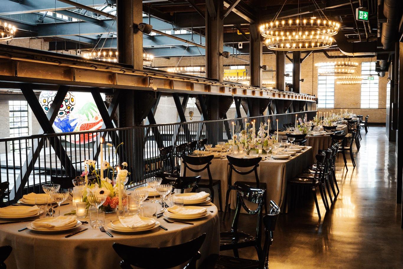 Seated dinner layout in the west hall. Tables with light gray linens, organic flower arrangements and tapers candles, are set for over 70 guests.