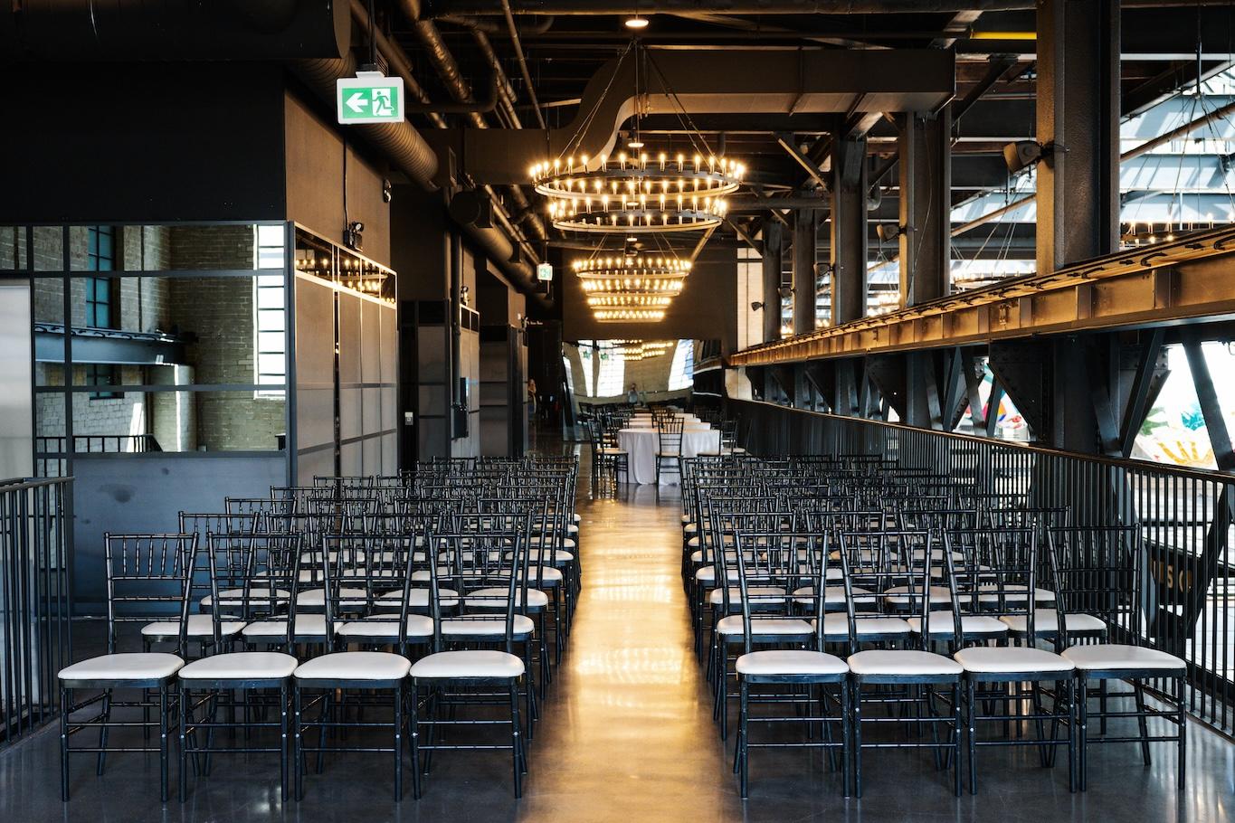 Meeting set up in the west hall showing rows of chairs beneath large two-tier steel chandeliers.