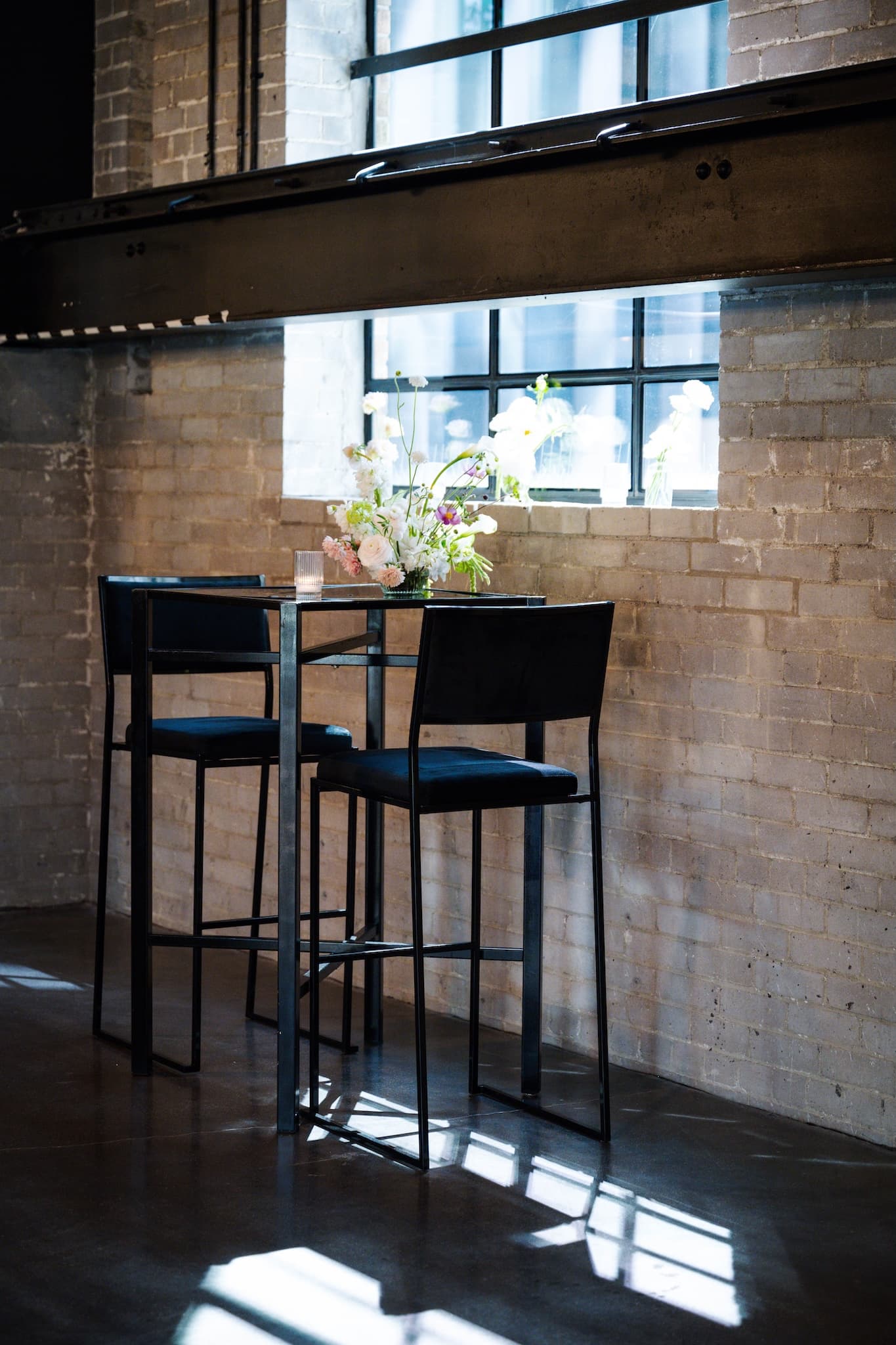 Black square cruiser table and two black chairs against the yellow brick wall.