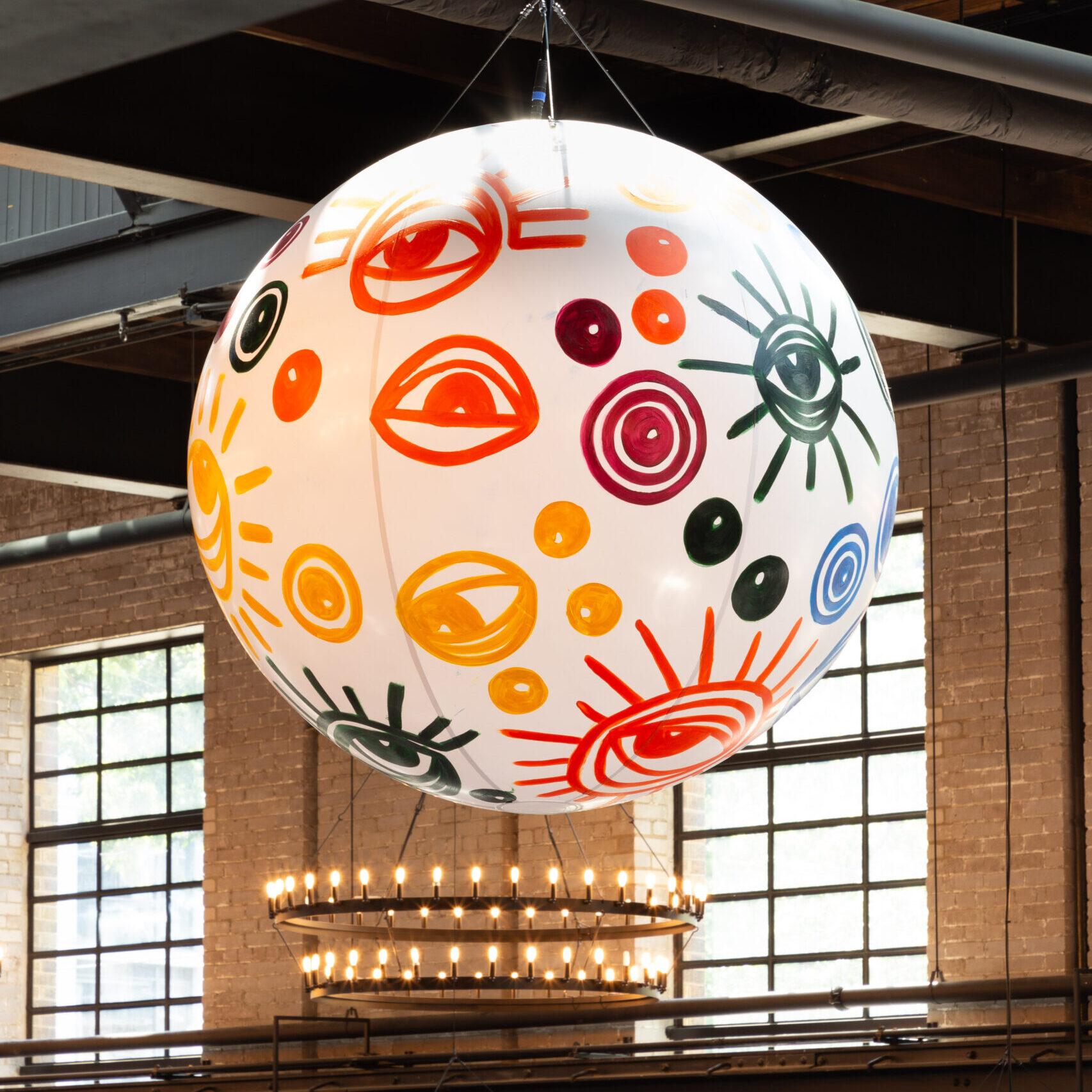 A large globe, painted with multi-coloured eyes, hanging from the ceiling of the food hall. The eyes on the sphere are a representation of the artist's ancestors and the people who walked before her.