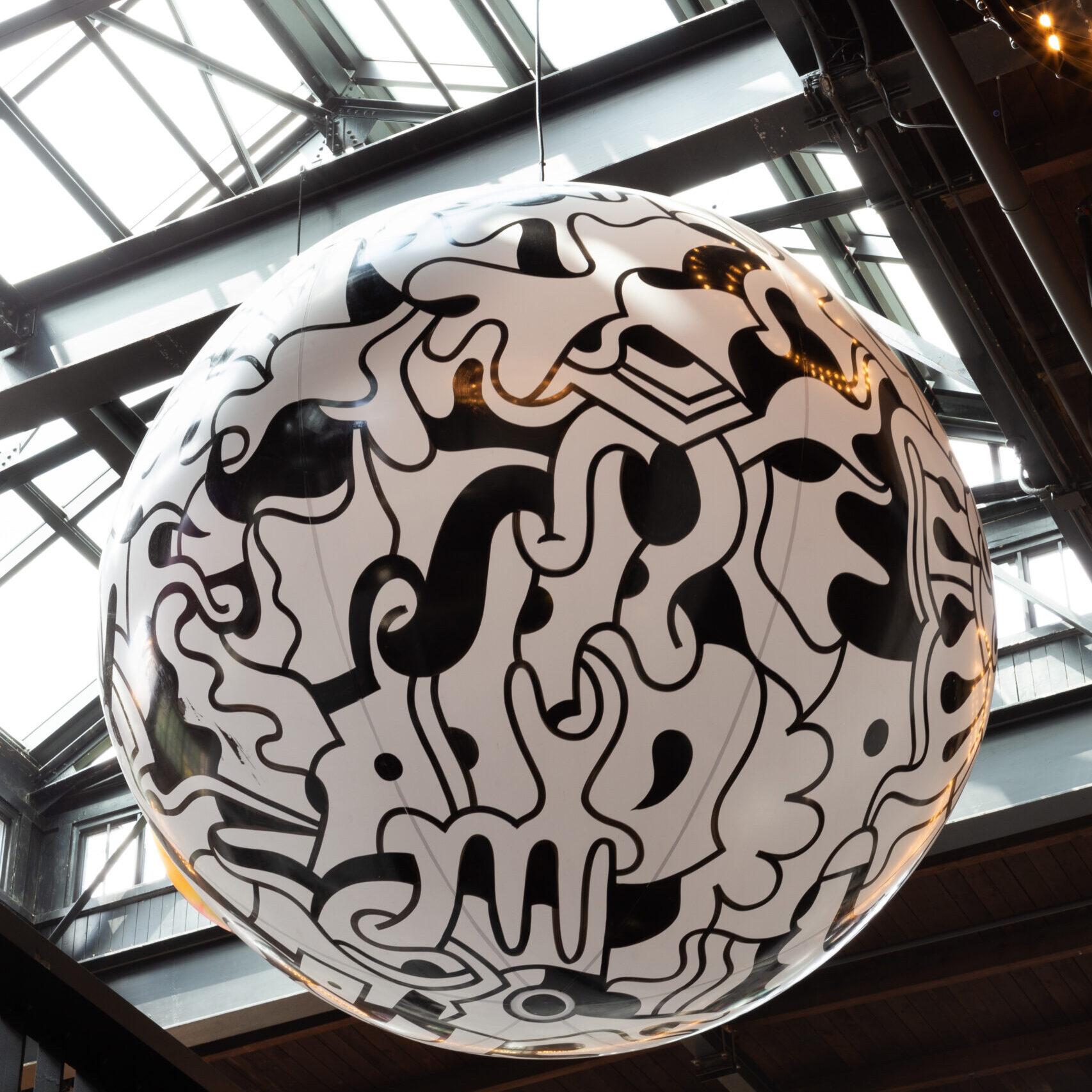 A monochromatic painted sphere hanging high in the rafters of the food hall.