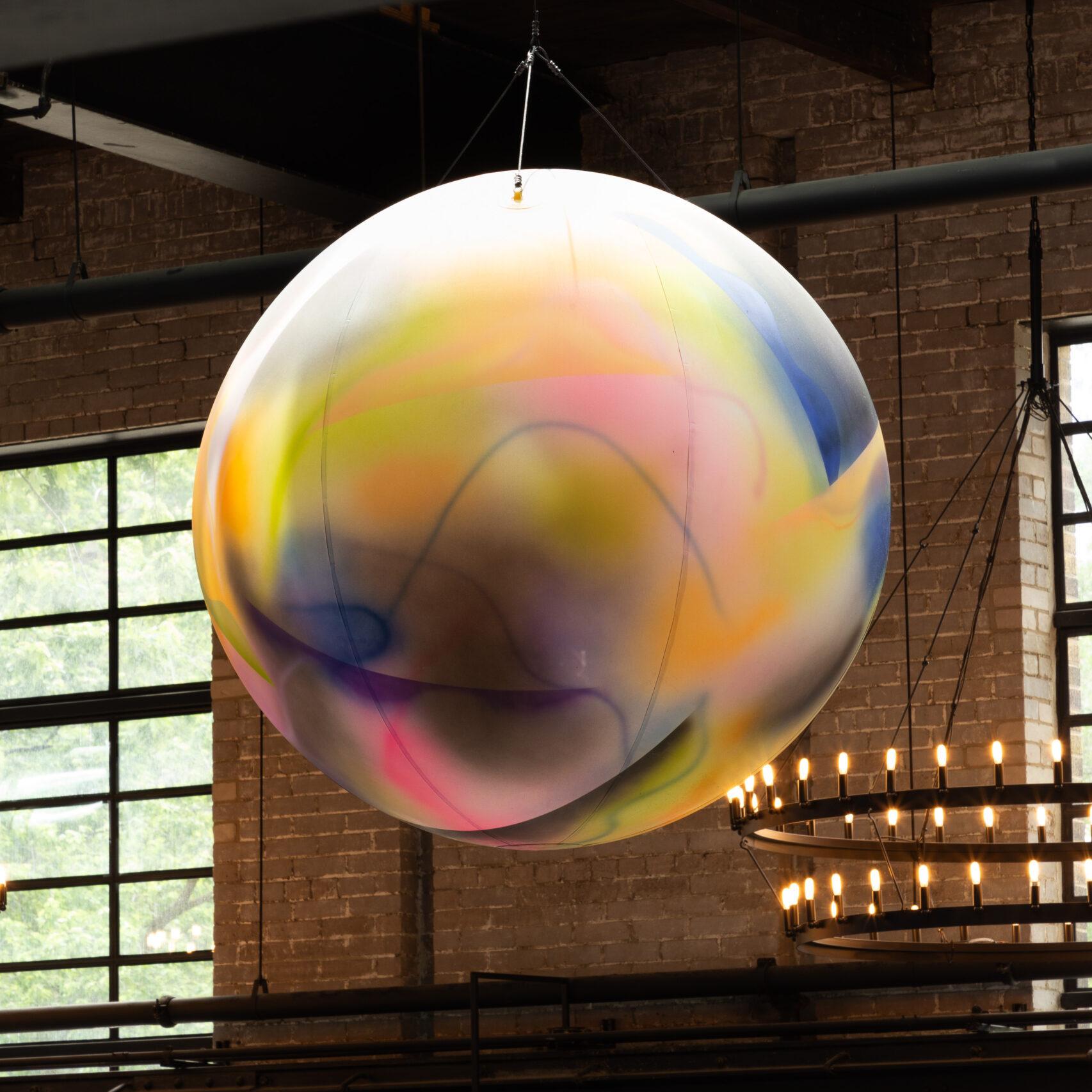 A smaller painted sphere, showing layers of soft colours, hanging from the rafters of the food hall.