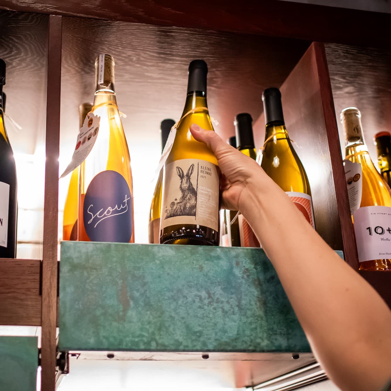 Person grabbing wine bottle from shelf