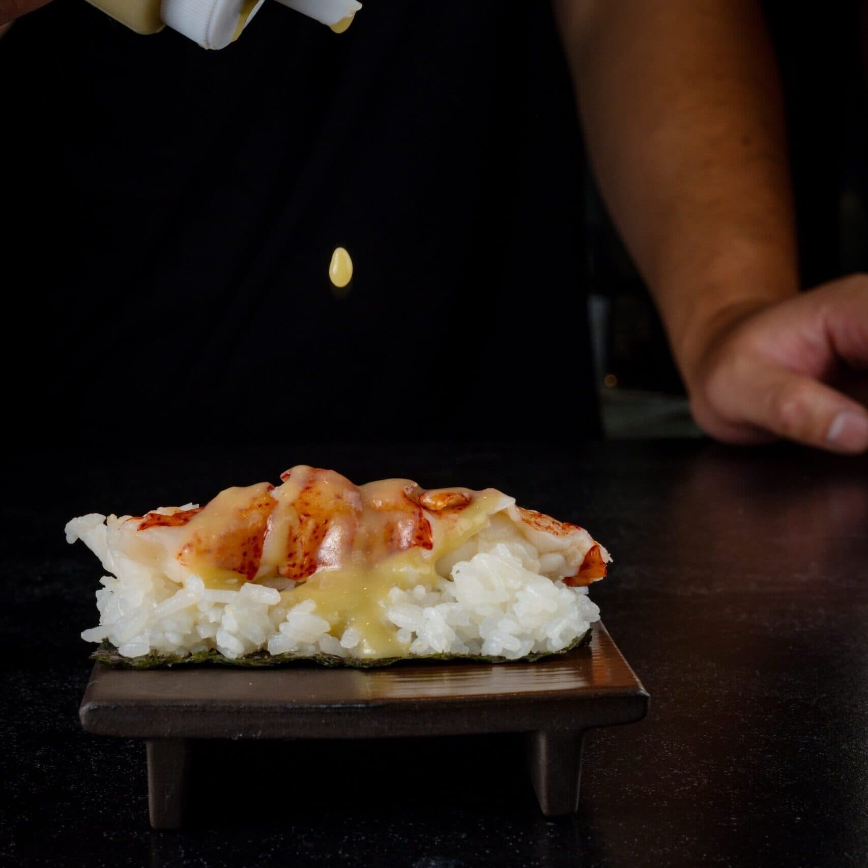 Chef adding drops of sauce to a lobster temaki hand roll.